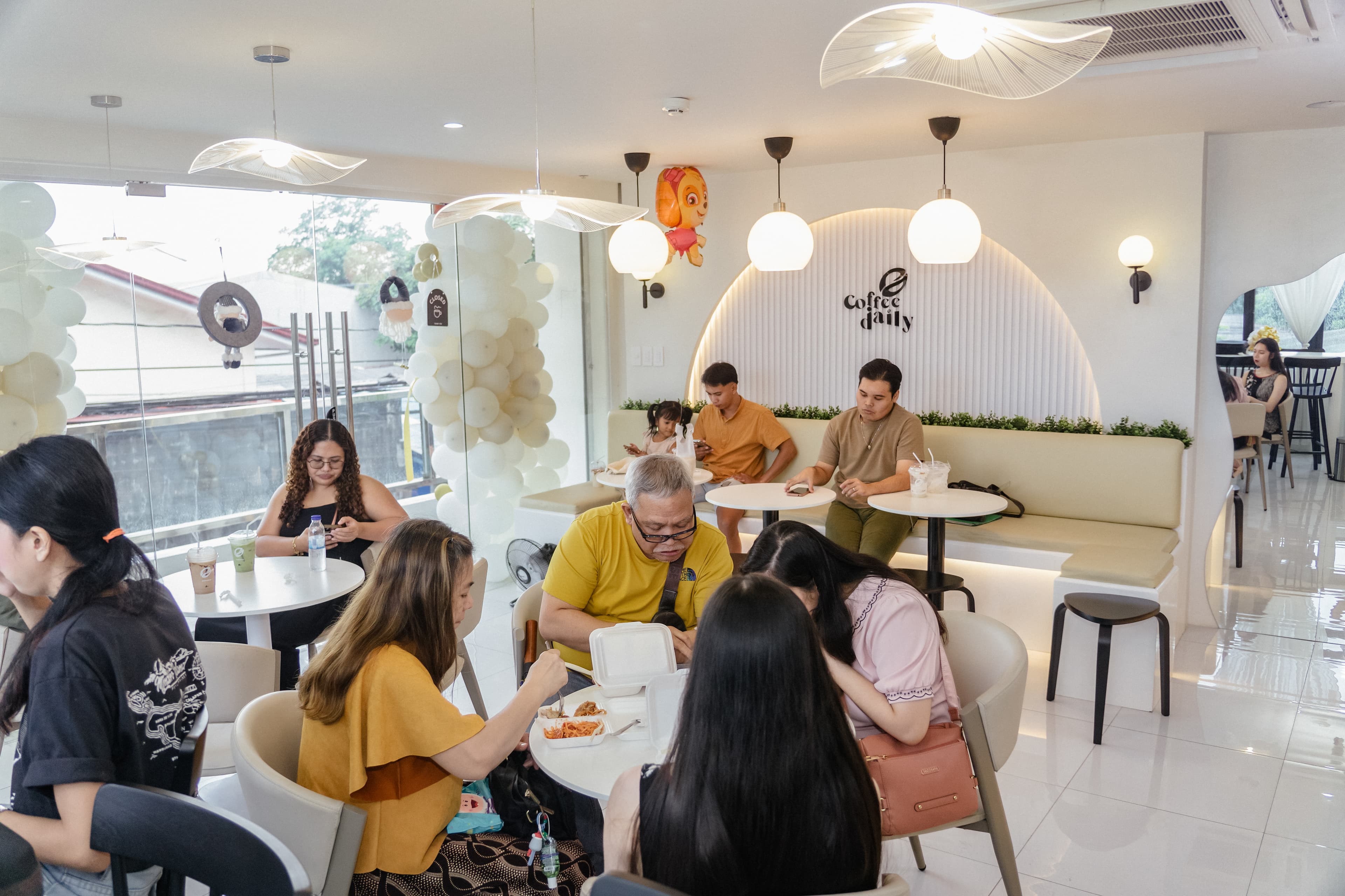 Customers dining and relaxing in a bright, modern cafe with white minimalist decor and lighting.
