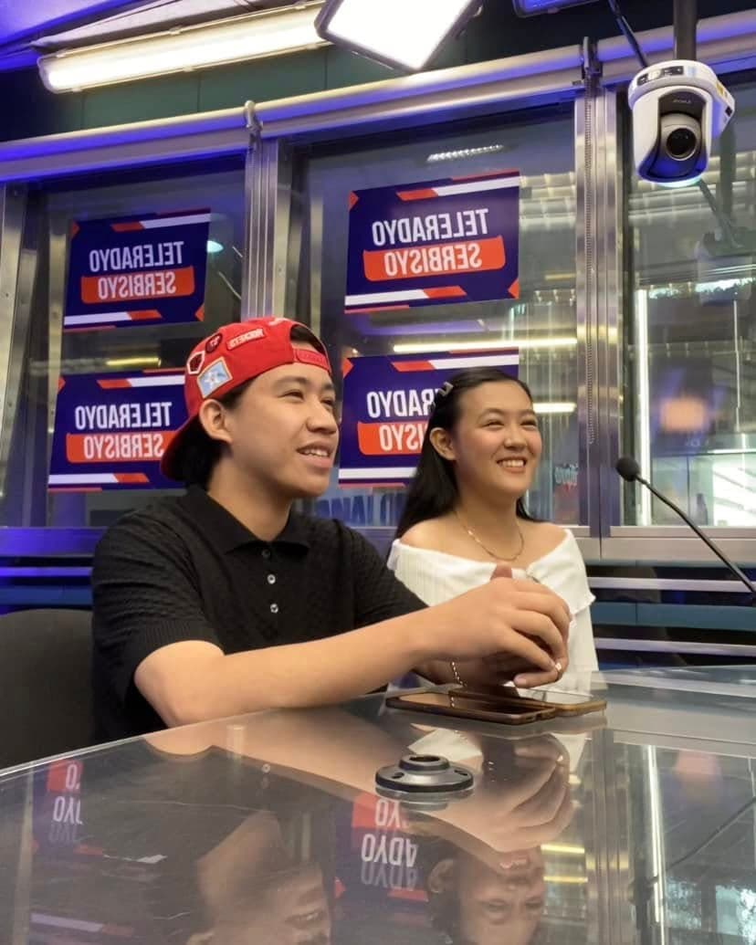 Smiling young man in a red cap and woman in white at a studio desk.