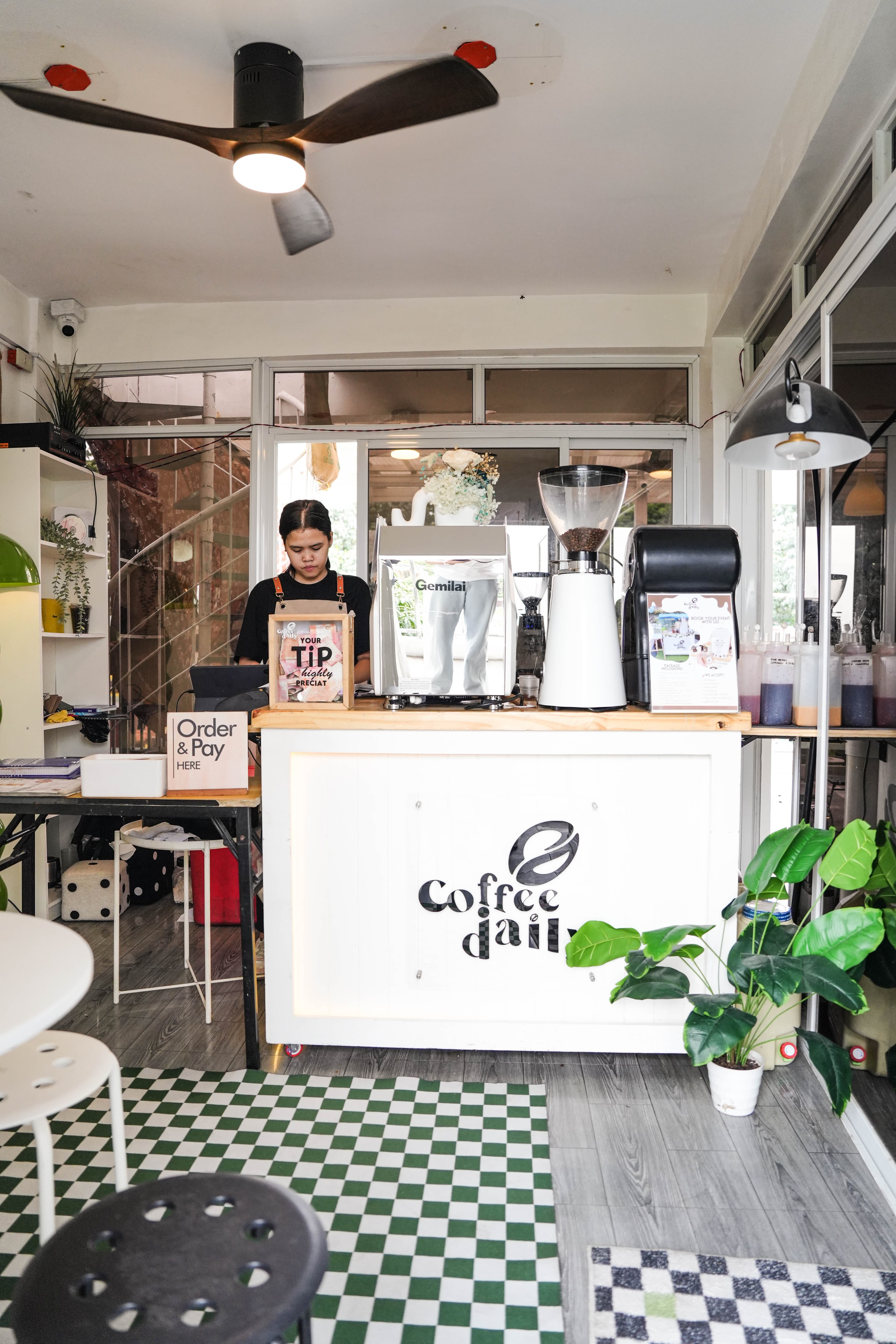 Barista behind a white Coffee Daily counter with an espresso machine and coffee grinder.