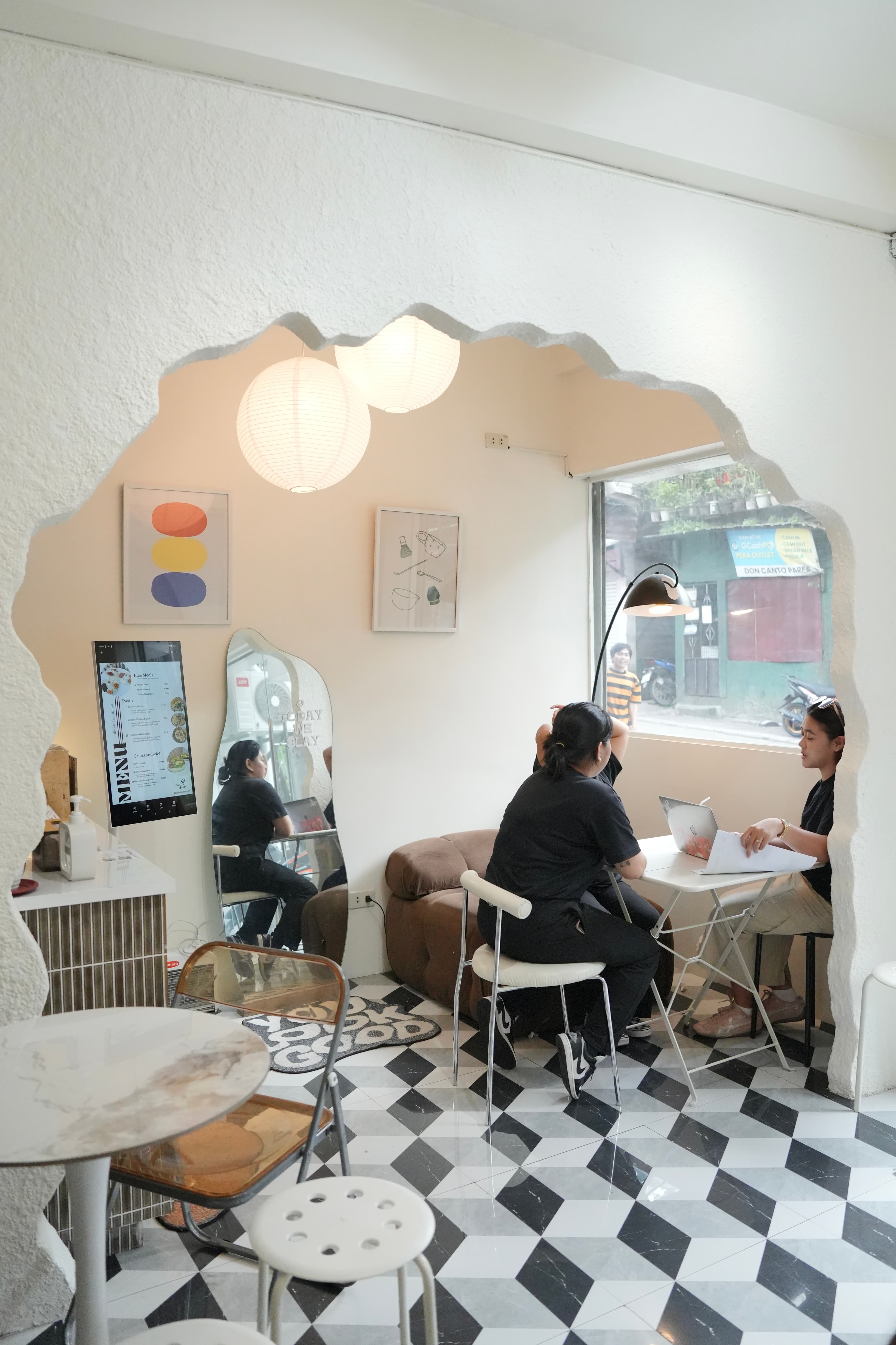 Modern cafe interior featuring a jagged archway, checkered floor, and people working at a table.