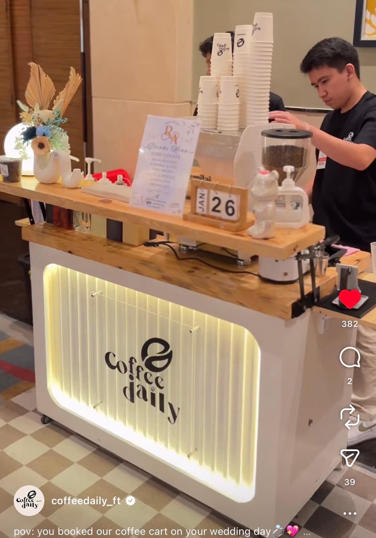 Barista at a white 'Coffee Daily' mobile cart with a backlit logo and wooden counter.