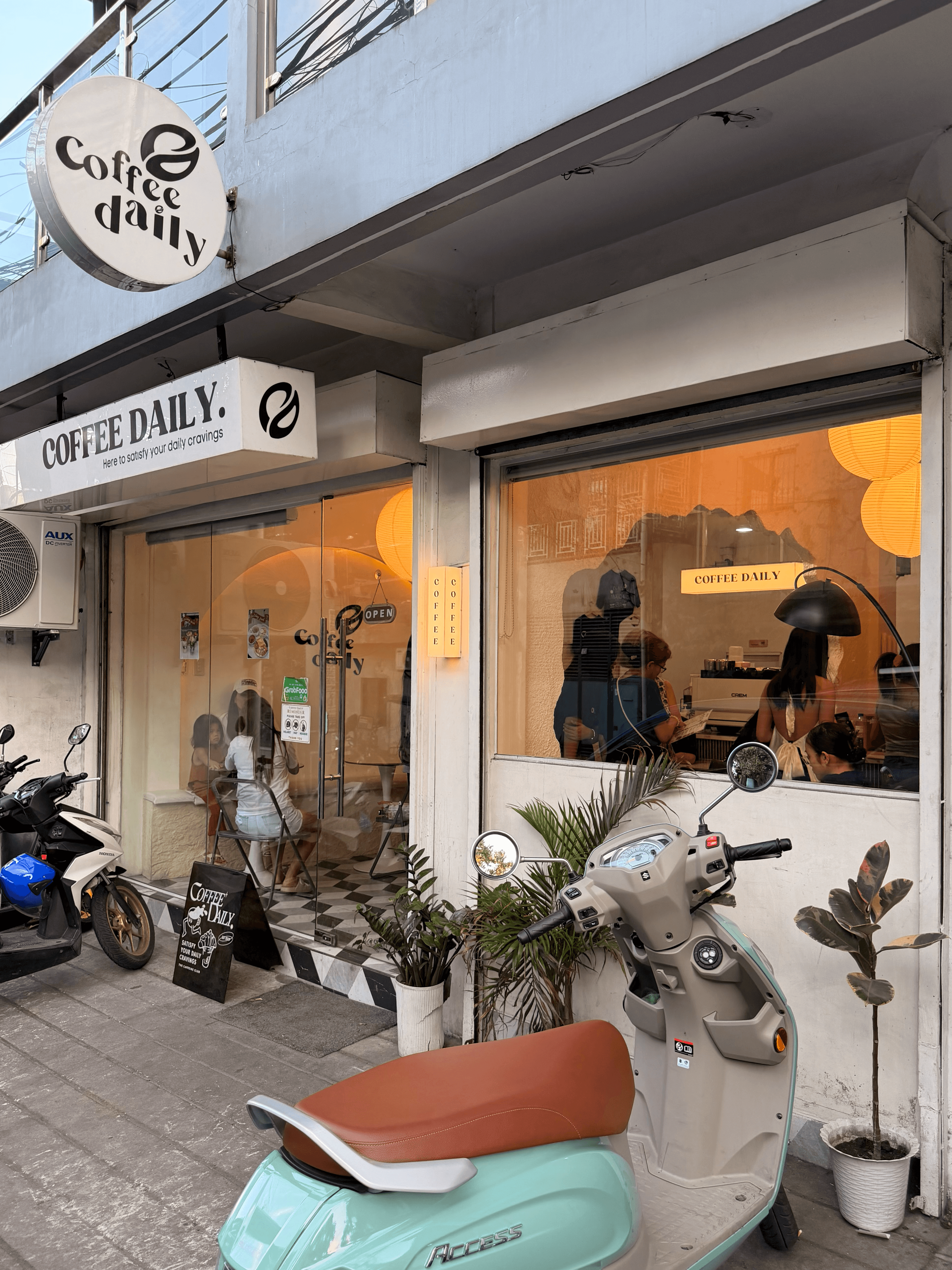 Coffee Daily storefront with large windows, patrons inside, and a mint green scooter parked.